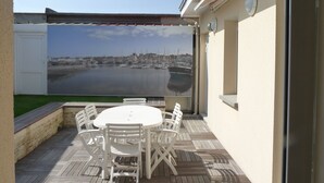 Une terrasse avec une table et des chaises, une vue sur une marina avec des bateaux, et un ciel dégagé.