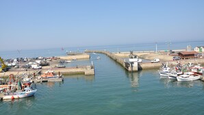 Un port où sont amarrés des bateaux, une jetée qui s’avance dans l’eau et un bâtiment avec un toit rouge.