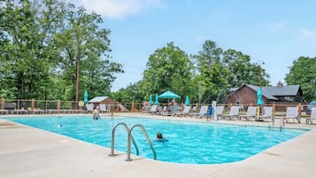 A swimming pool with lounge chairs and umbrellas, surrounded by trees and a wooden building.