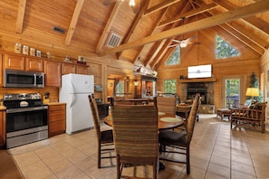 A spacious kitchen with modern appliances, a dining area with a large wooden table and woven chairs, and a cozy fireplace. - Secluded Cabin, HotTub, Jet Tub, Woods, Near Big Cedar & Shows-Firepit -Car Charger (Ridgedale)
