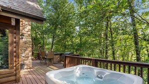 Une terrasse en bois avec un jacuzzi, des murs en pierre et du mobilier d’extérieur.