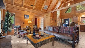 L’intérieur d’un chalet confortable, avec un plafond en bois, un canapé, une table basse et un coin repas comprenant des chaises et une table.
