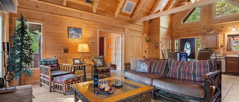 Un acogedor interior de cabaña de madera con techo de madera, un sofá, una mesa de centro y un comedor con sillas y una mesa.