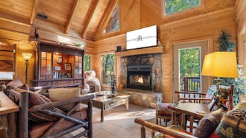 A cozy log cabin interior with a stone fireplace, wooden furniture, and a bear statue.