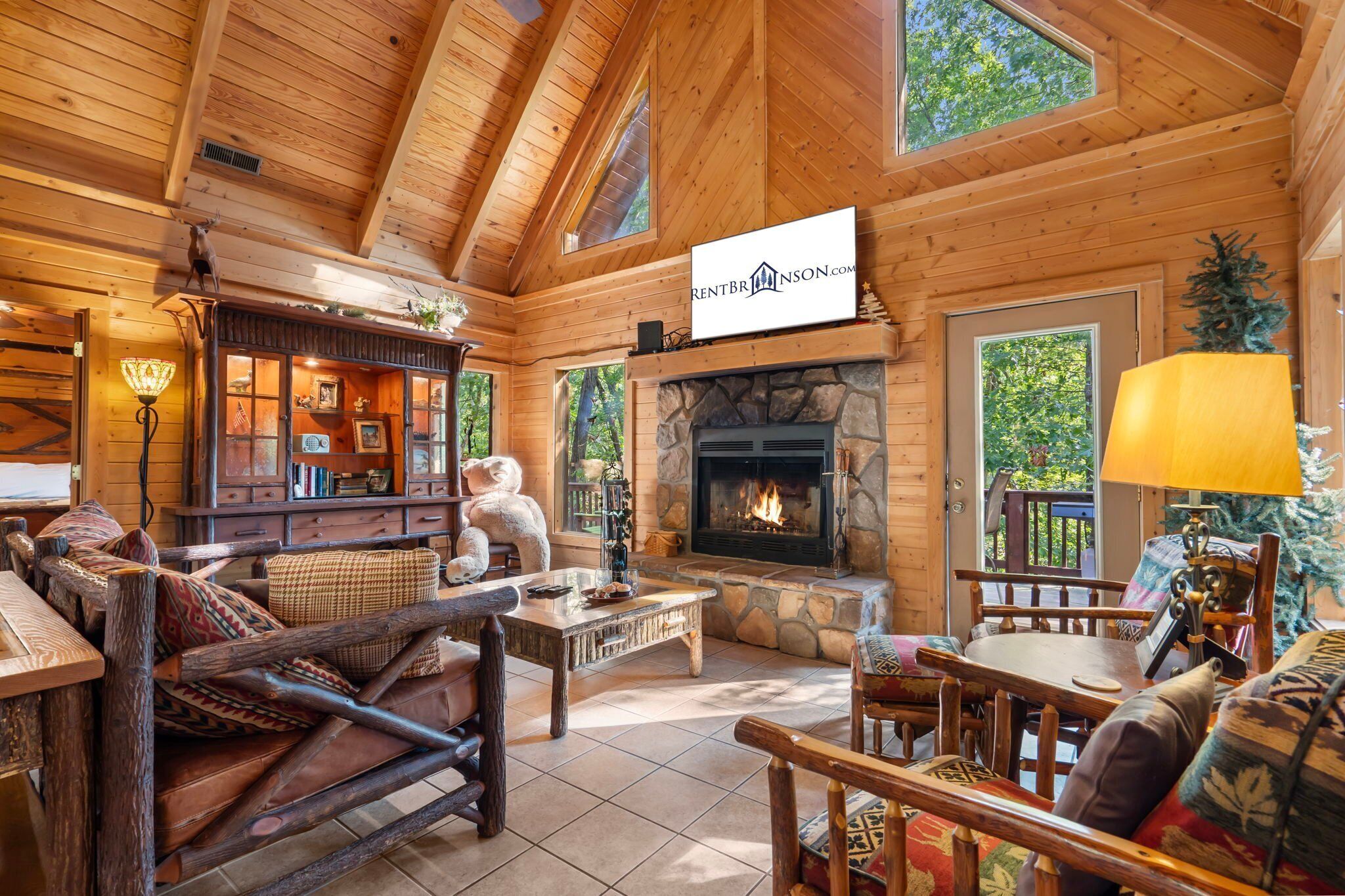L’intérieur chaleureux d’un chalet en bois, avec une cheminée, des meubles en bois et une enseigne indiquant « RentBrinson.com ».