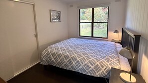 Ein Schlafzimmer mit Bett, Fenster, Nachttischlampe und einem Bild an der Wand.