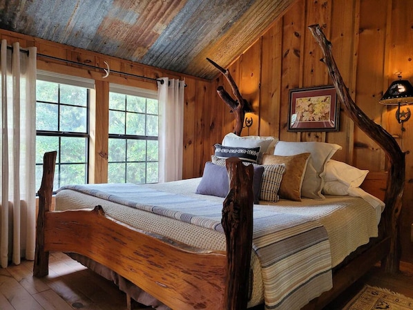 A rustic wooden bedroom with a large bed, a wooden headboard, and a window with curtains.