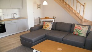 A modern living room with a grey sectional sofa, a wooden coffee table, and a kitchen area with white cabinets and a sink. - 3 The Courtyard Award Winning 4 Star Vineyard Gite (Monbadon)