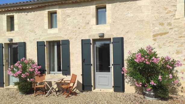 A stone building with two windows, a door, and a small patio area with a table and chairs. - 3 The Courtyard Award Winning 4 Star Vineyard Gite (Monbadon)