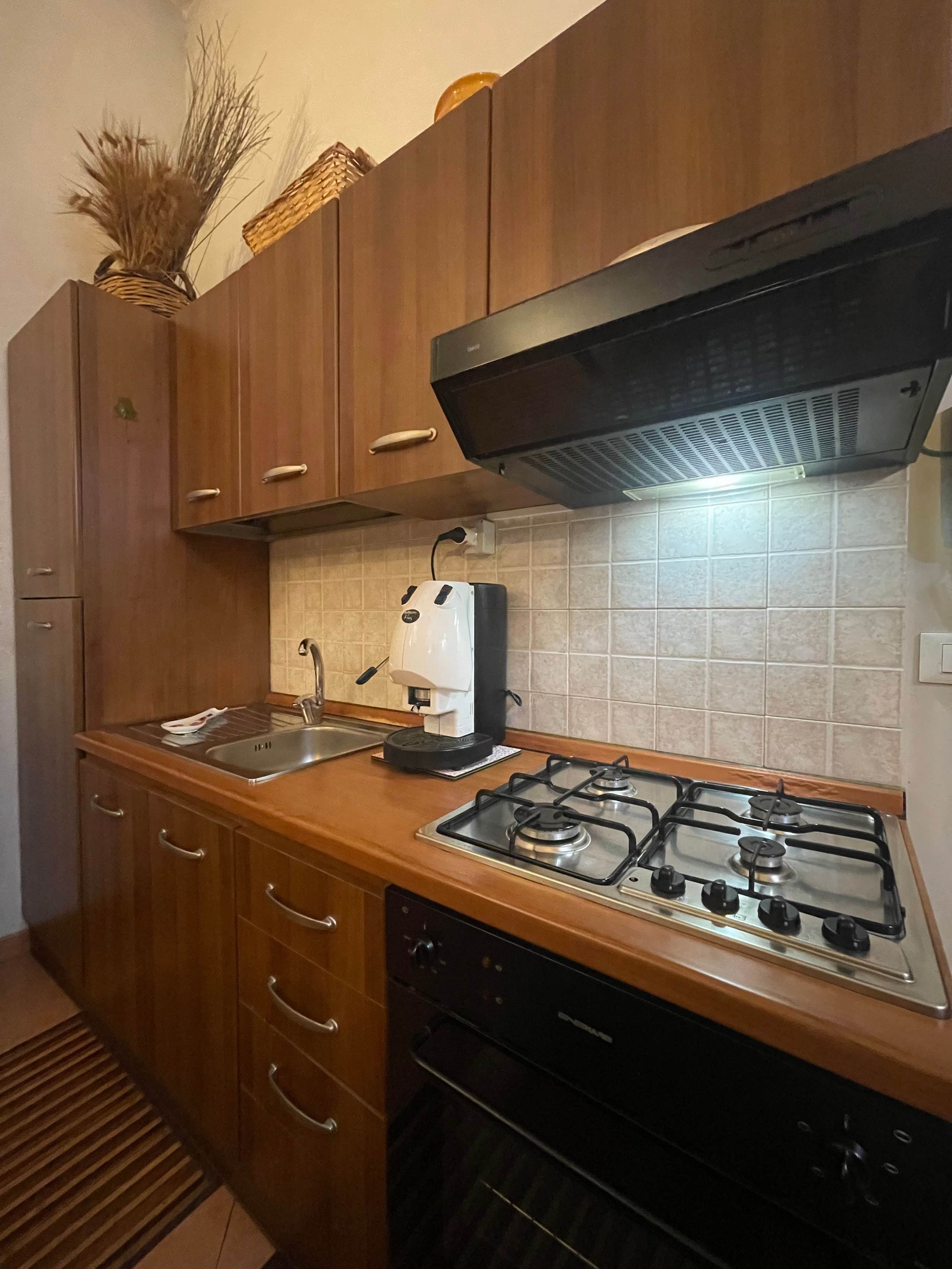 A kitchen with wooden cabinets, a gas stove, a coffee maker, and a sink.