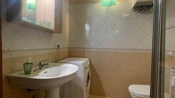 A bathroom with a sink, mirror, washing machine, and toilet.