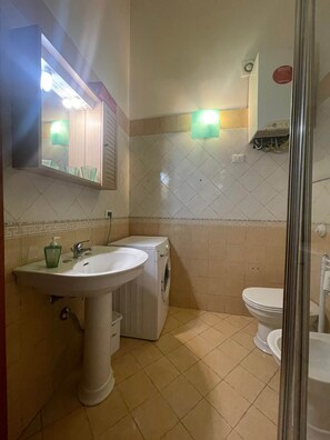 A bathroom with a sink, mirror, washing machine, and toilet.