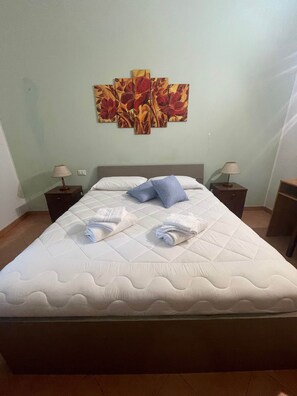 A hotel room with a bed, two nightstands, a wall art piece, and a folded towel on the bed.