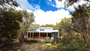 A modern house with a covered porch, surrounded by dense trees and a dirt path. - Three Bedroom Bushland House (Anglesea)