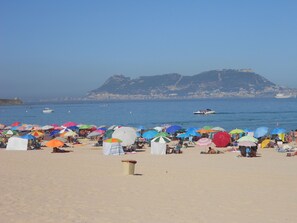 Une plage avec de nombreux parasols colorés et des gens qui prennent un bain de soleil.