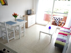 A small, bright room with a white table, chairs, a sofa, and a TV on a wooden cabinet. - apartment at the beach of Getares with roomsbikeanddive (Algeciras)