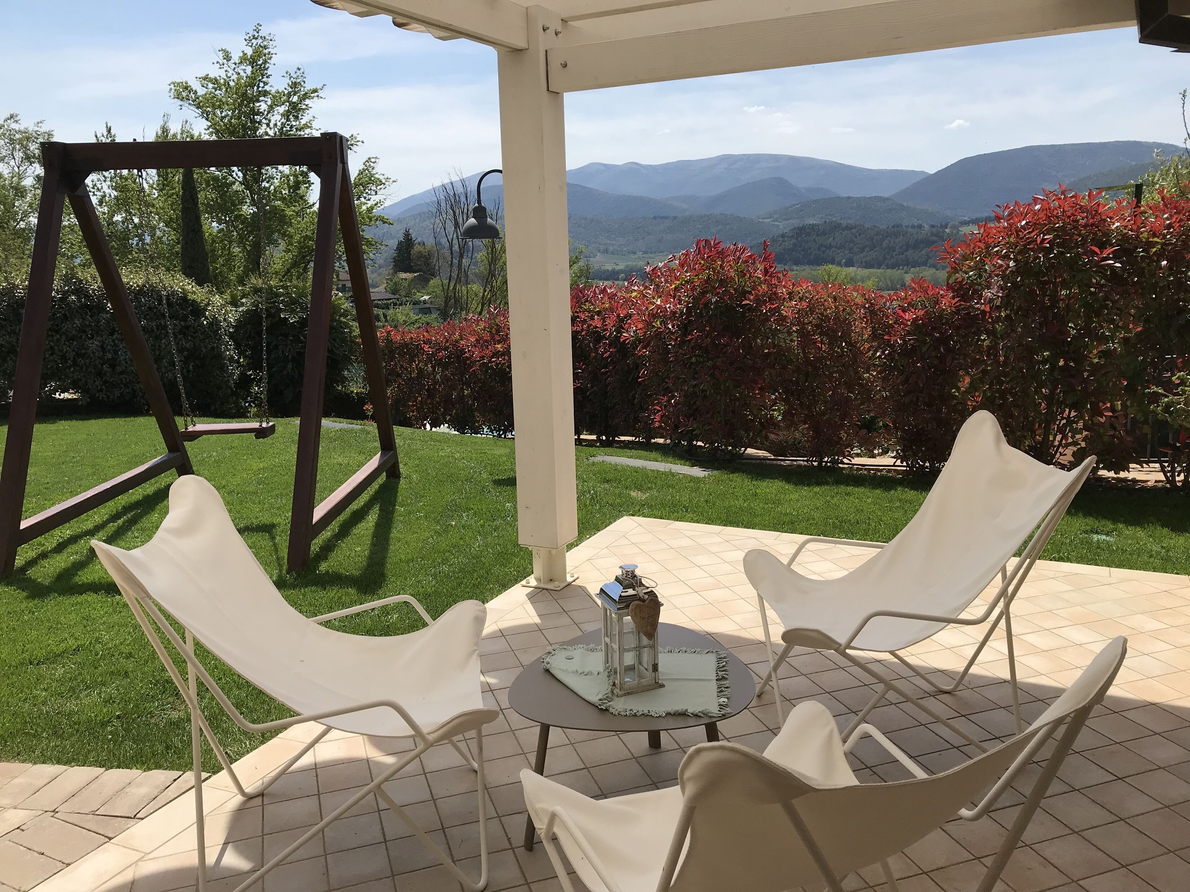 A patio with a swing set, white chairs, and a table with a lantern.