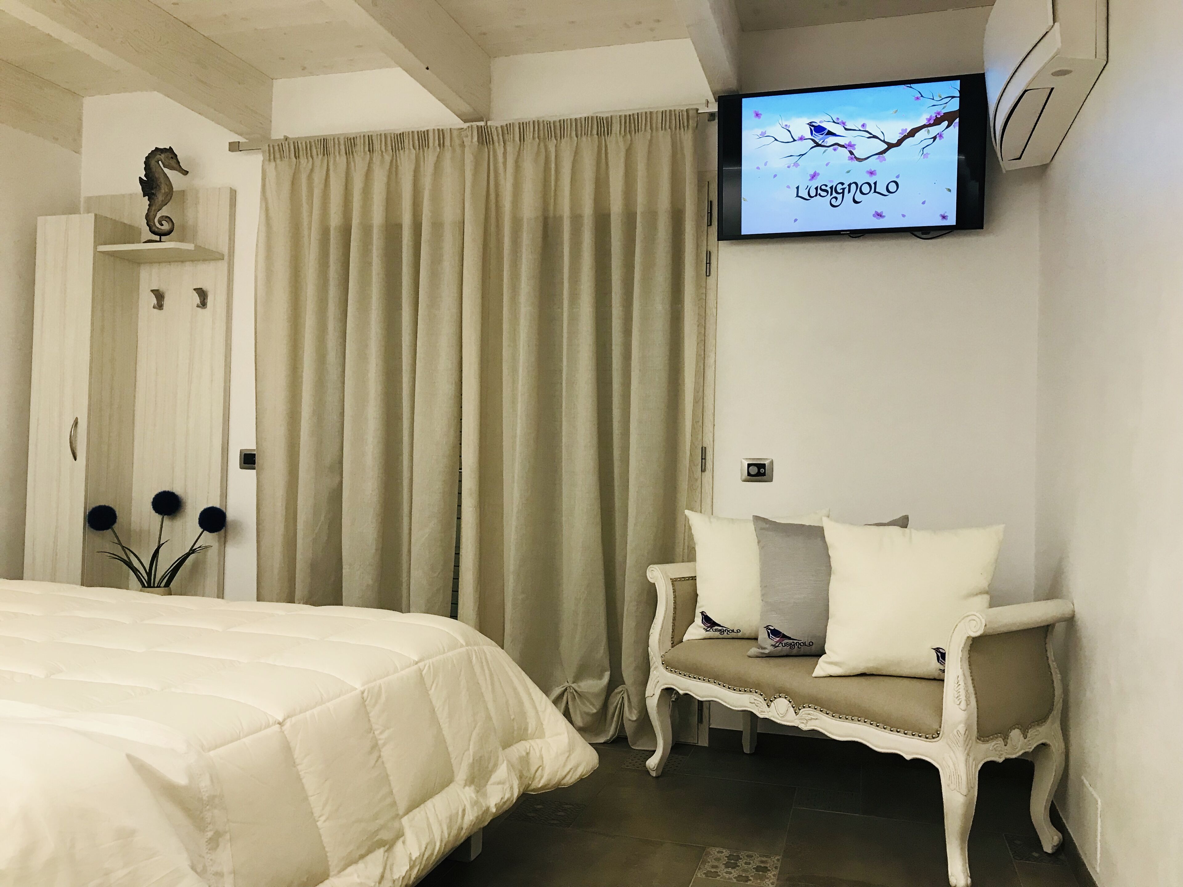 A bedroom with a bed, a bench, a television, and a curtain.