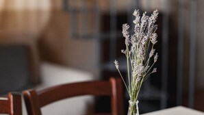 A dining table with a clear glass vase containing lavender flowers, set on a white tablecloth.
