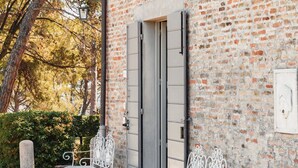 A brick building with a door and two white metal chairs outside.