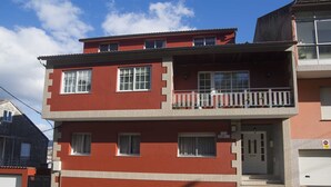Edifici de dues plantes amb façana vermella, un balcó al pis superior i una porta de garatge a la dreta.
