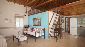 A spacious living room with a high wooden ceiling, a sofa, a coffee table, and a staircase leading to an upper level. - Eleni's Charming Cottage, ideal for Couples or Families seeking Natural Living (Skiathos island)