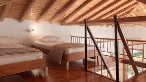 A high-ceilinged attic bedroom with wooden beams, two beds, a nightstand, and a staircase. - Eleni's Charming Cottage, ideal for Couples or Families seeking Natural Living (Skiathos island)