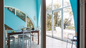 A dining area with a table and chairs, a staircase, and large windows offering a view of the outdoors. - Beautiful villa overlooking the beach of Seccione (PORTOFERRAIO)