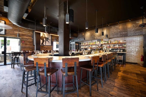 Zona de bar con una barra alargada, varios taburetes y una pared de ladrillo con un menú.
