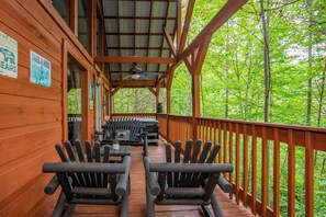 Eine Holzterrasse mit Adirondack-Stühlen und einem Tisch, umgeben von einem Wald.