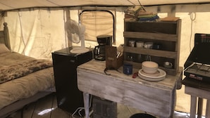 A compact, rustic tent interior with a bed, a fan, a coffee maker, and a shelf with dishes and a propane stove. - Glamping Tent at the base of the mountains outside Joseph, Oregon at Evans Farm. (Joseph)