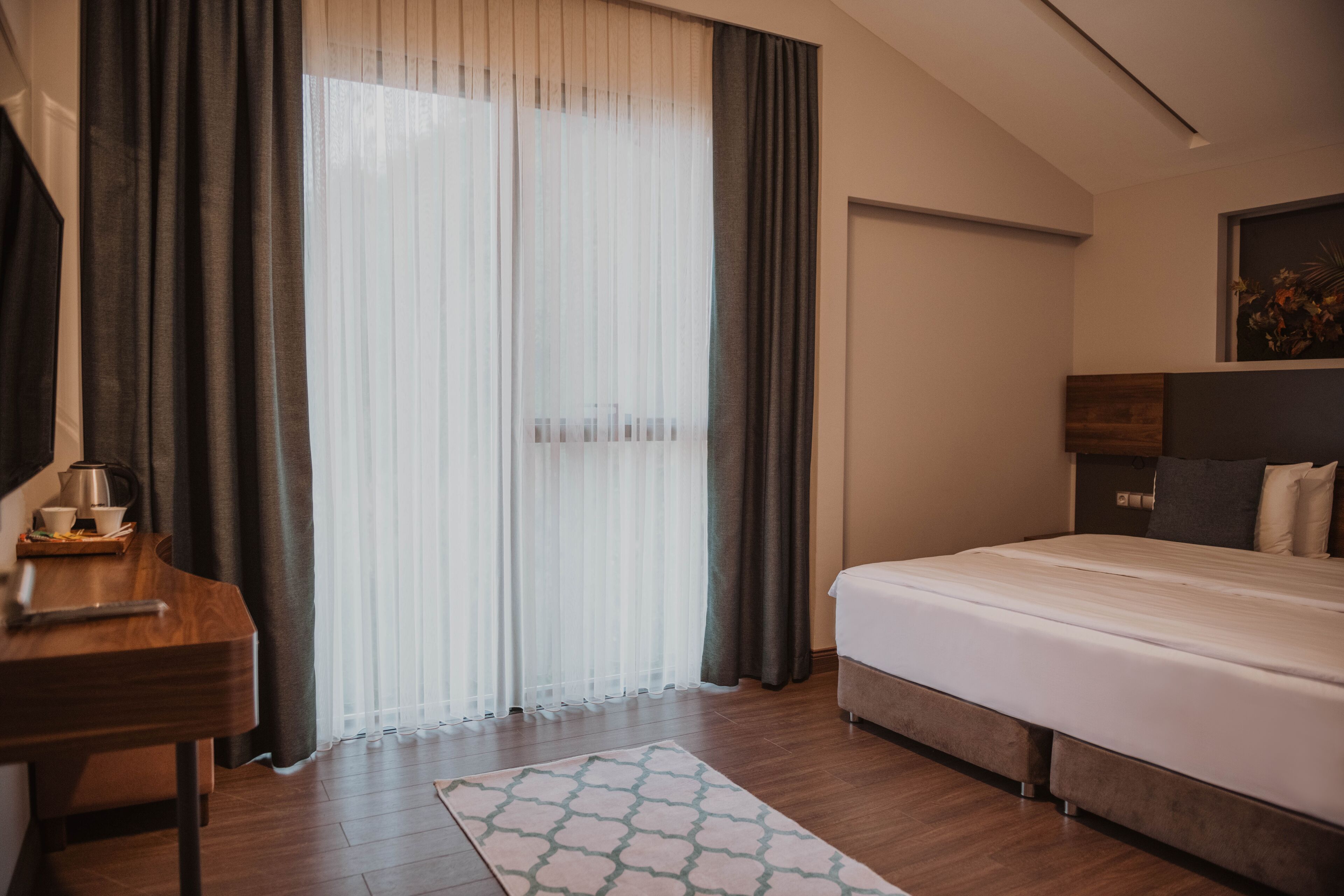 Una habitación de hotel con cama, escritorio, cafetera y ventana con cortinas.