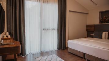 Una habitación de hotel con cama, escritorio, cafetera y ventana con cortinas.