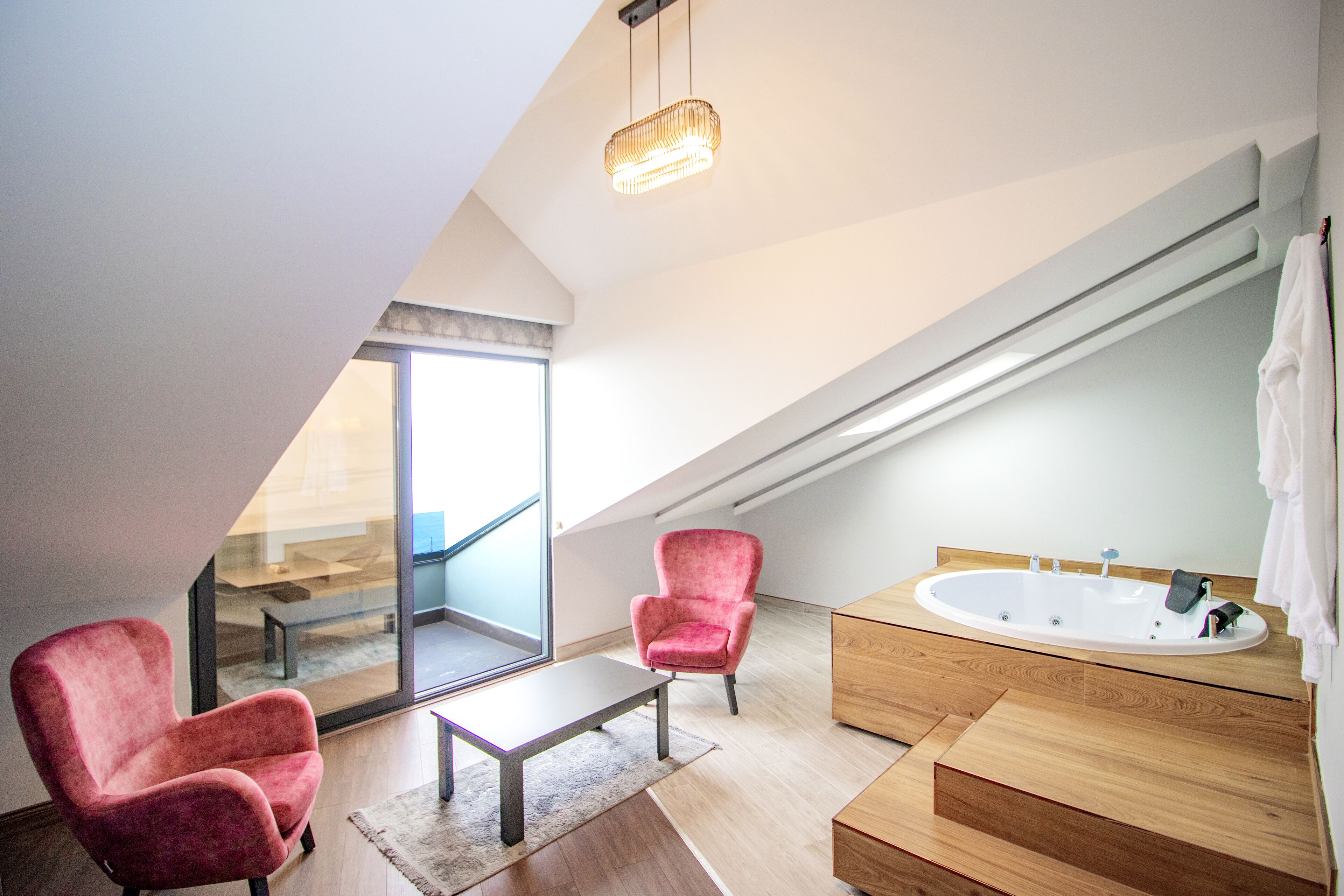 A modern bathroom with a freestanding bathtub, two red armchairs, a wooden vanity, and a large mirror.