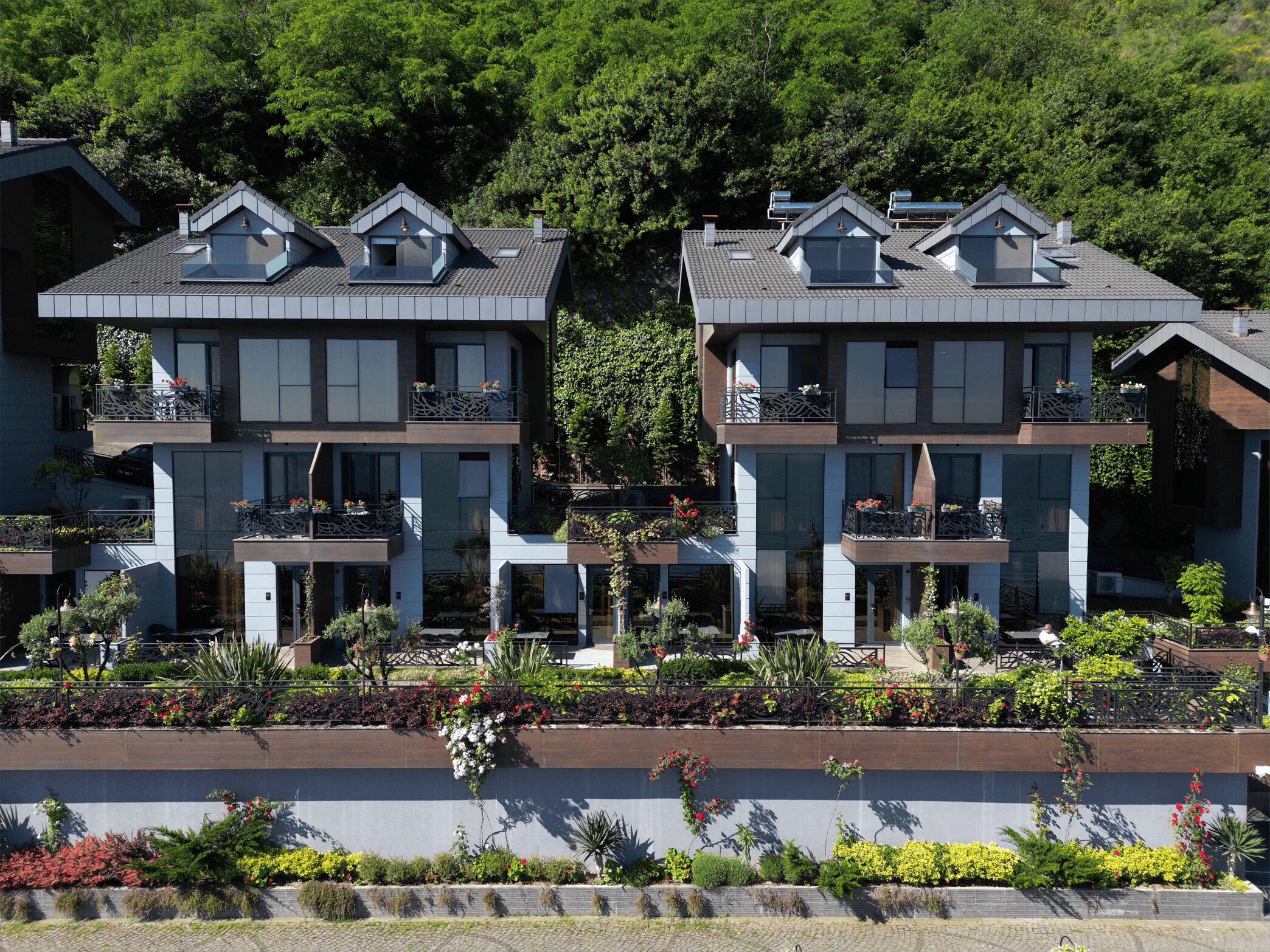 Um edifício moderno de vários andares, com varandas, um telhado plano e um jardim ajardinado.