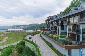 A hotel with multiple balconies, a paved walkway, and a view of a cityscape and hills in the background. - Peerless Villas Hotel (Trabzon)