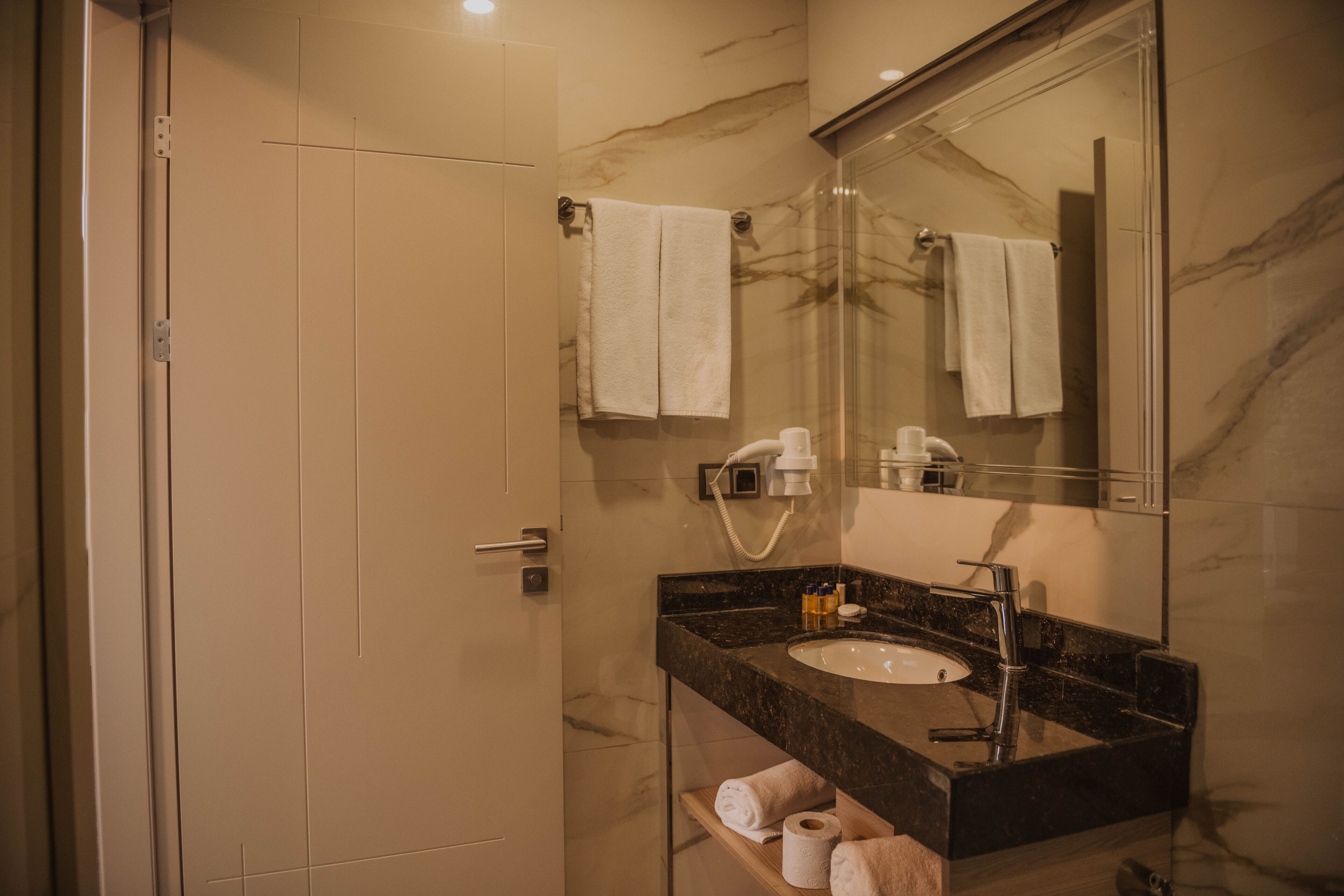 A modern bathroom with a marble wall, a sink with a mirror, and a shower area.