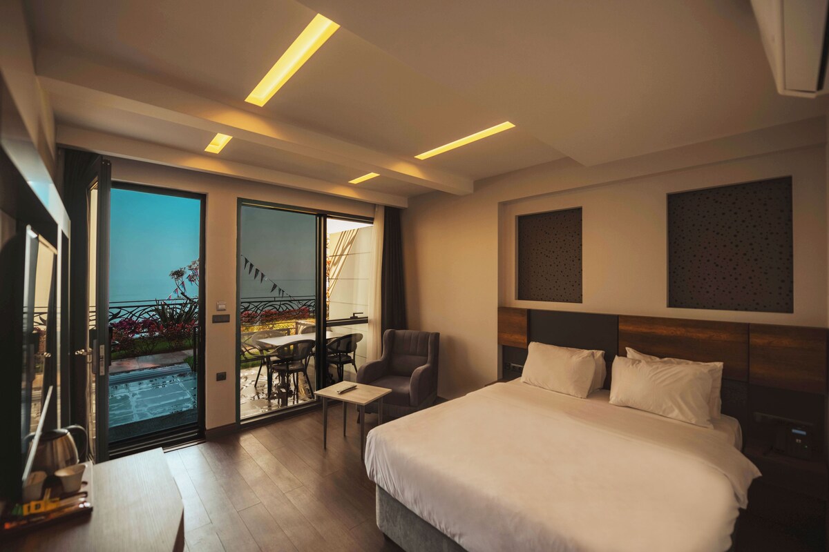 Habitación de hotel moderna con una cama grande, una mesita, una silla y un balcón con mobiliario de exterior.