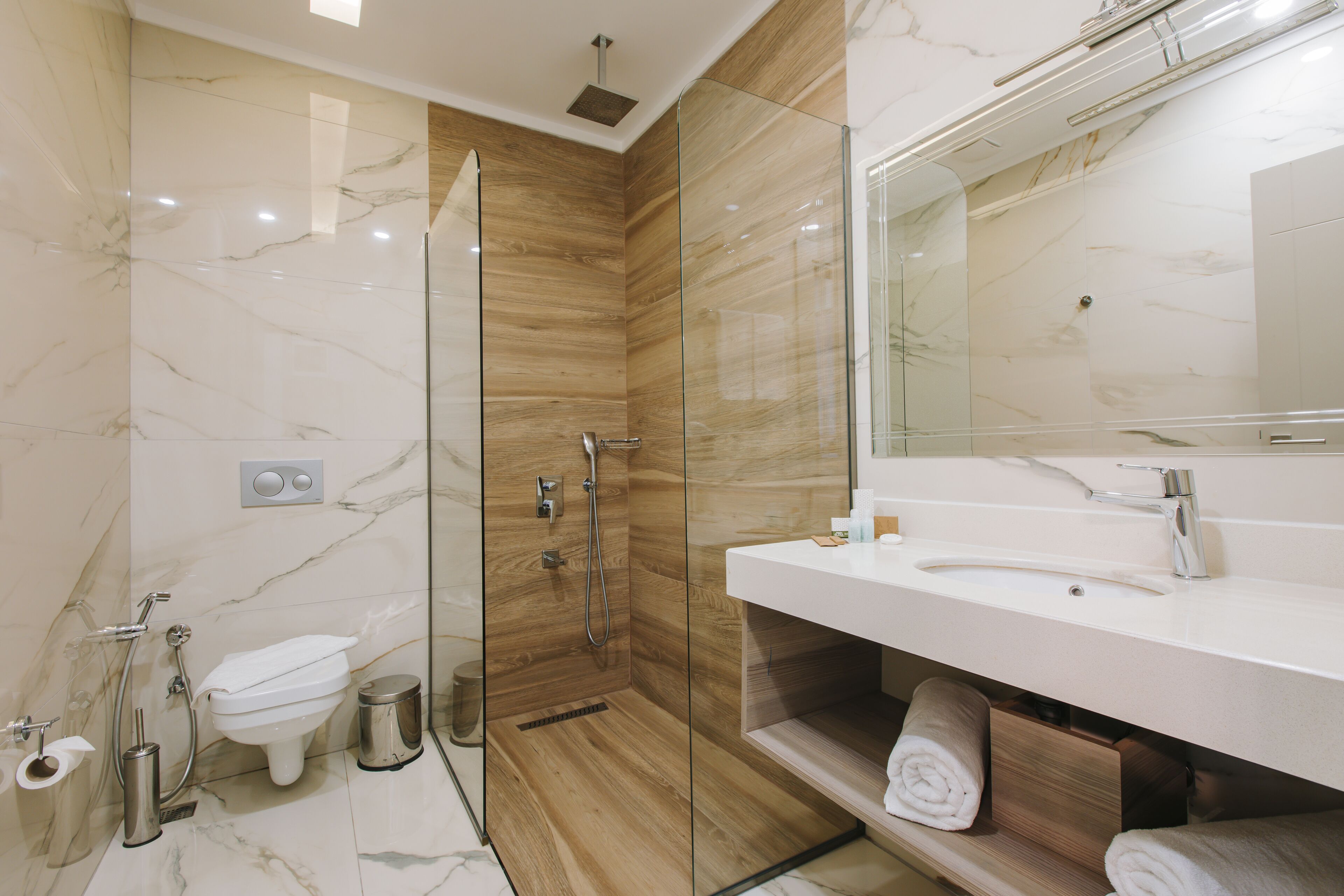 Une salle de bain moderne avec une douche à parois de verre, un lavabo blanc et un pare-baignoire en marbre.