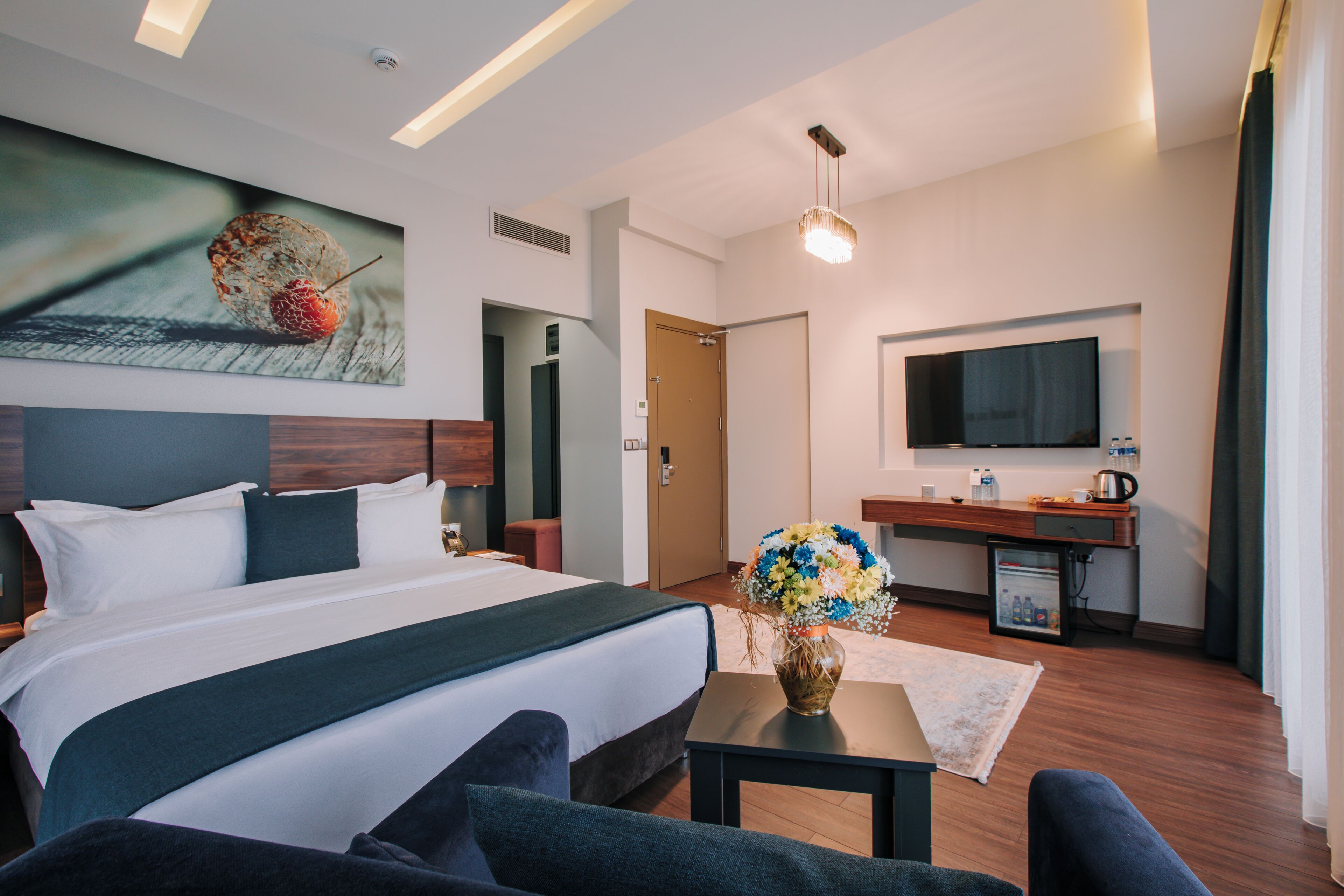 Una habitación de hotel moderna con una cama grande, un escritorio, un televisor de pantalla plana y un cuadro en la pared.