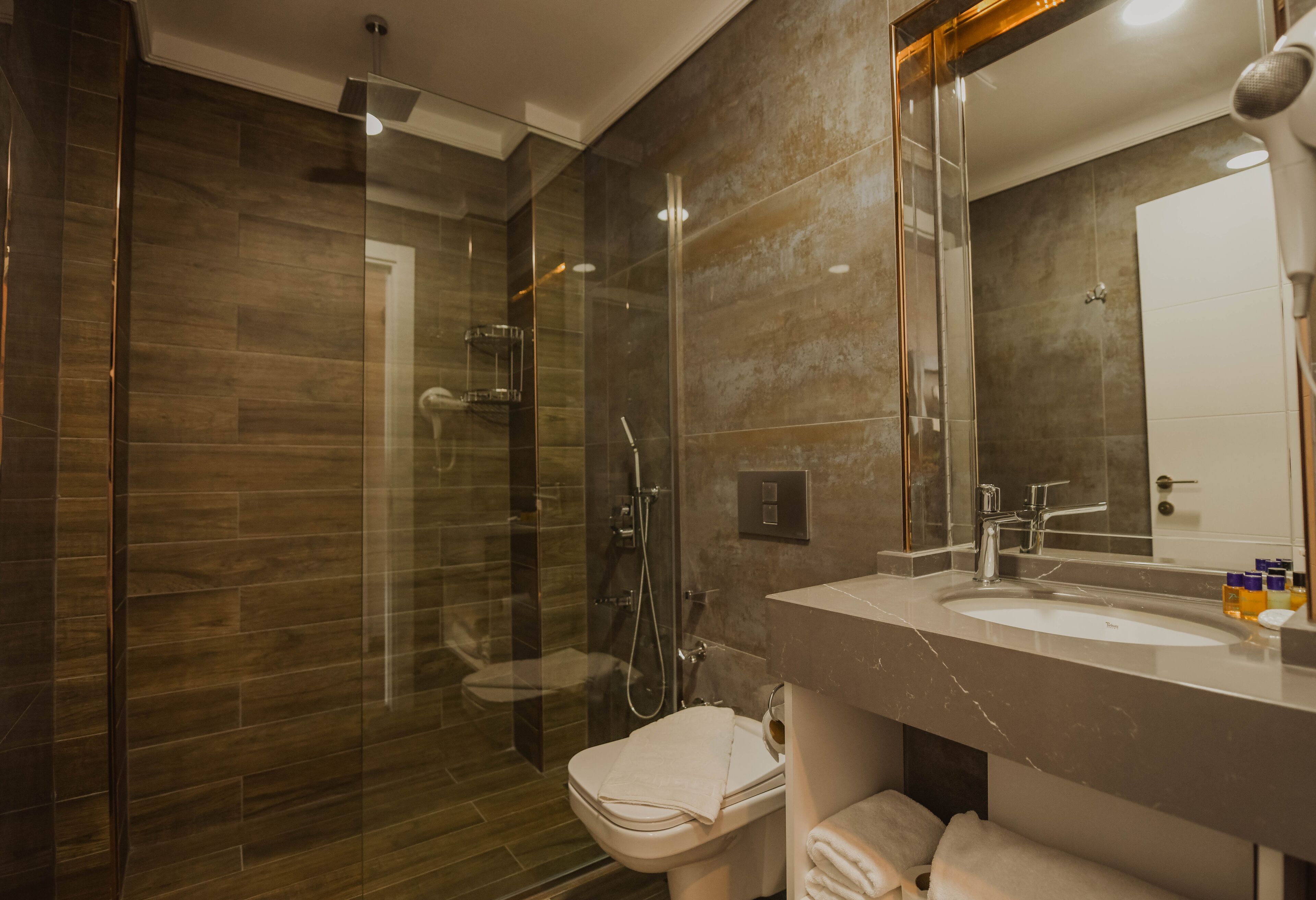 Ein modernes Badezimmer mit einer begehbaren Glasdusche, einem Marmorwaschtisch und einem großen Spiegel.
