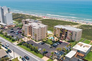 A coastal hotel with multiple buildings, a parking lot, and a beach view.