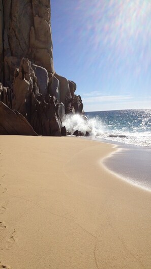 A beach with a rocky cliff and waves crashing onto the shore.