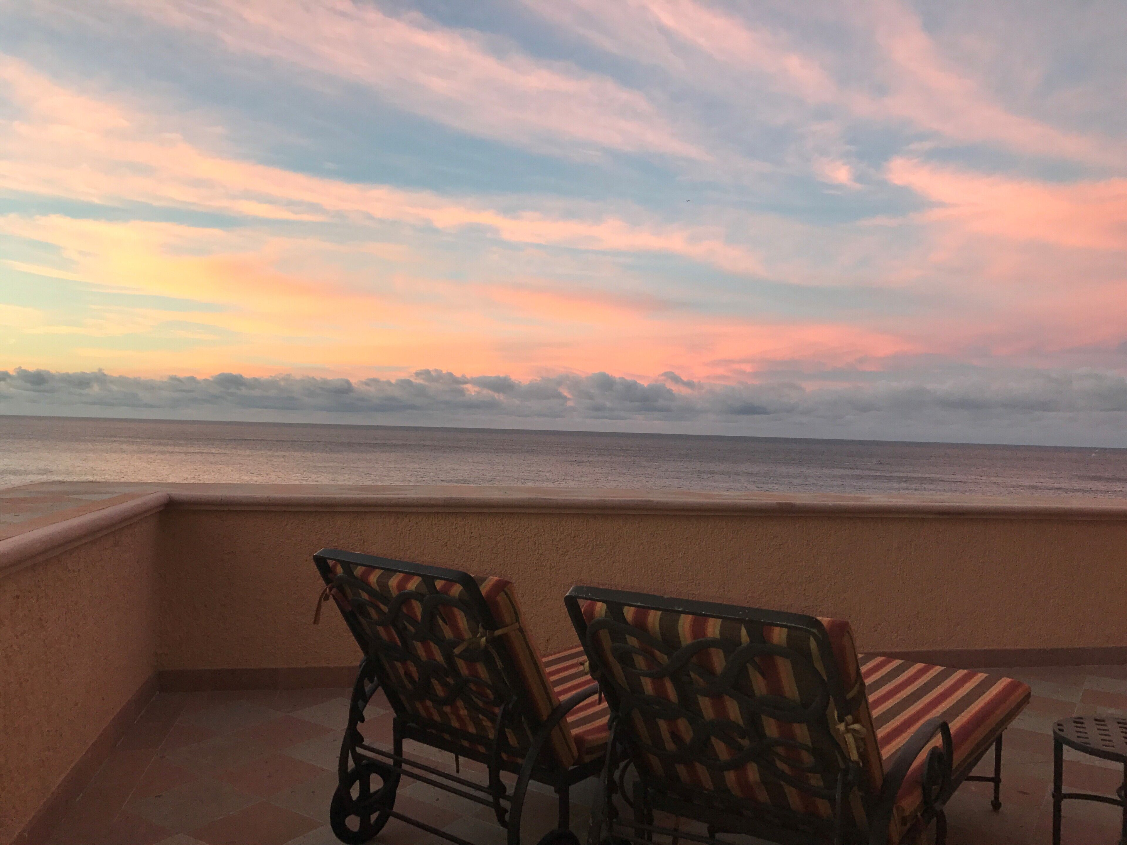Varanda com duas cadeiras voltada para um pôr do sol sobre o oceano.