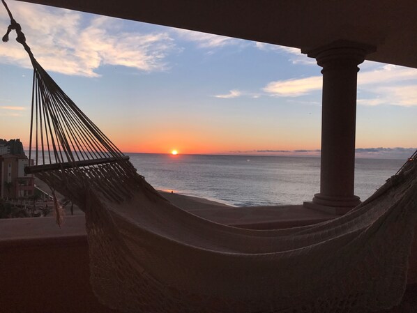 A hammock overlooking a sunset view of the ocean.
