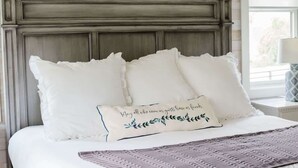 Un lit avec une literie blanche et des coussins décoratifs, un plaid texturé et une tête de lit en bois foncé.