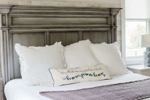 Een bed met witte beddengoed, decoratieve kussens, een zachte deken en een hoofdbord van donker hout.