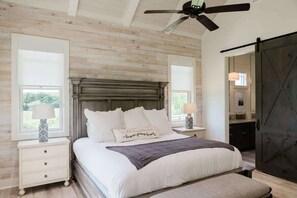 Une chambre avec un plafond en bois, un lit recouvert de linge de lit blanc, deux tables de chevet avec des lampes et une porte coulissante de style grange.