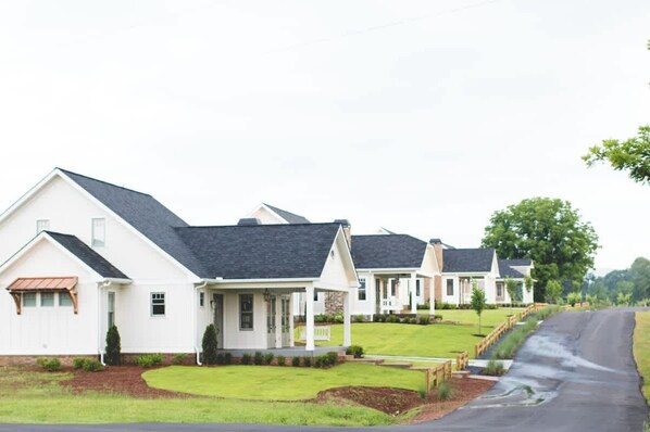 A row of white houses with dark roofs, a grassy lawn, and a paved driveway.