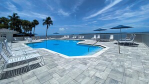 Ein Poolbereich mit Liegestühlen, Sonnenschirmen, Palmen und blauem Himmel.